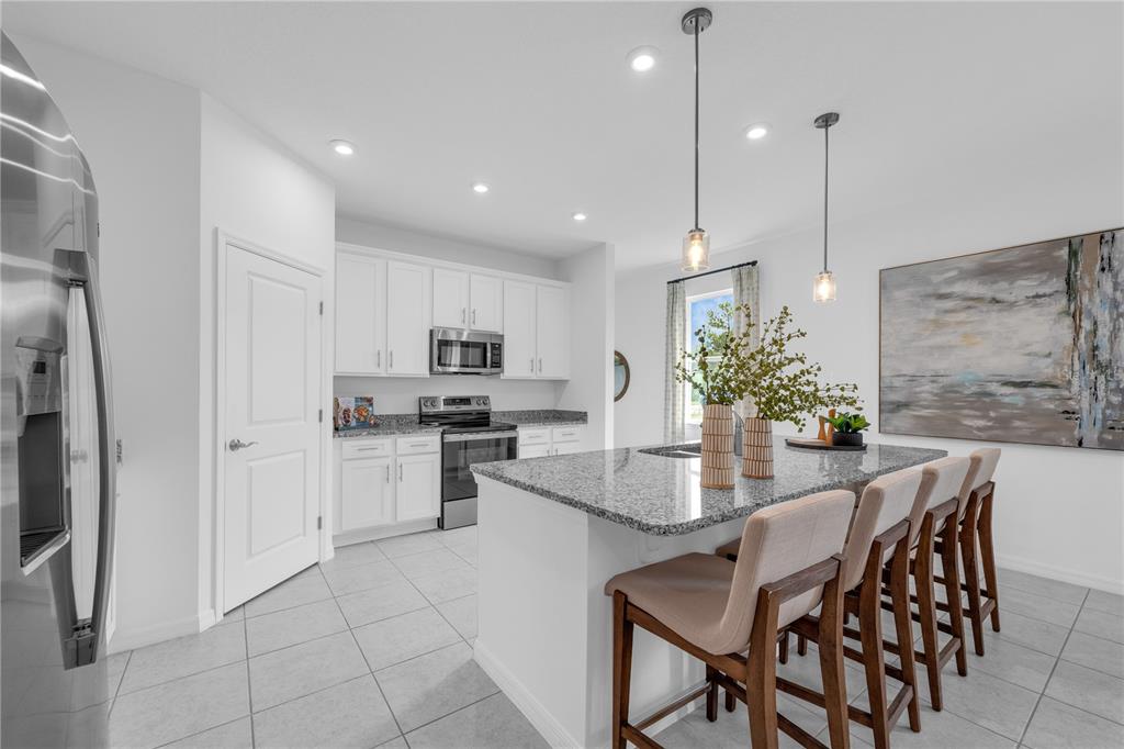 A kitchen features white cabinets, granite countertops, a center island with seating, and tile flooring — 10123 MORNING MEADOWLARK TRAIL, PARRISH, FL