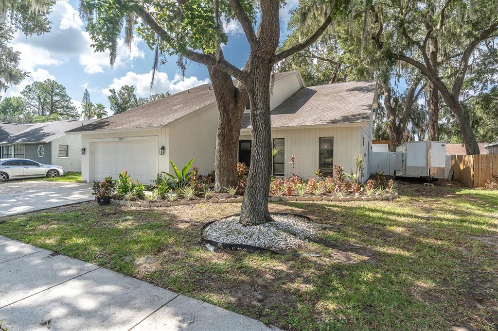 A white single-story house with a two-car garage and large trees in the front yard — 1901 LANDSIDE DRIVE, VALRICO, FL