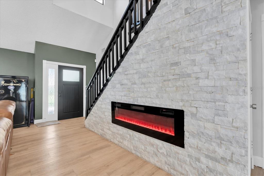 A modern living room features a stone-clad wall with a built-in electric fireplace and staircase — 1901 LANDSIDE DRIVE, VALRICO, FL