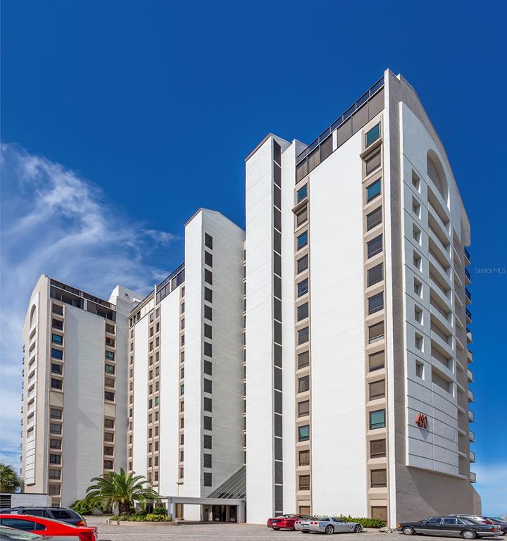 A tall, white multi-story residential building stands under a clear blue sky — 440 S GULFVIEW BOULEVARD UNIT 1705, CLEARWATER BEACH, FL