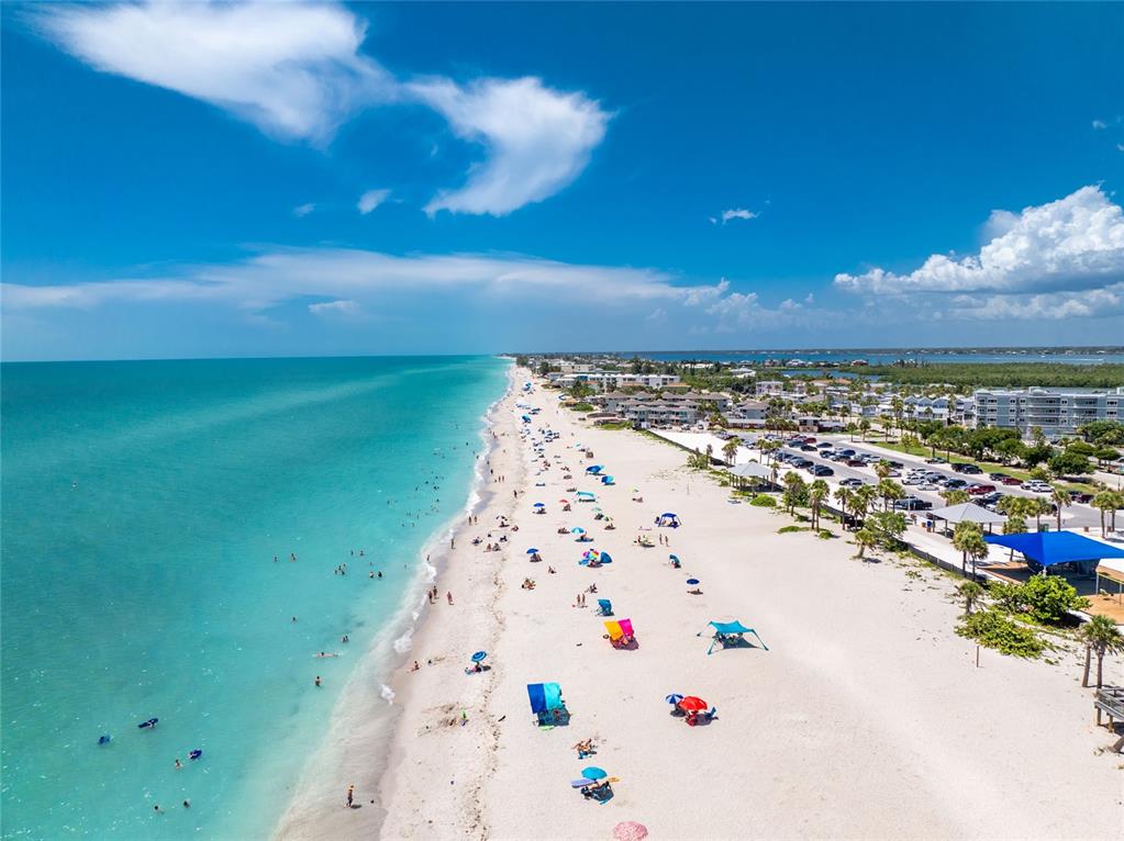 An aerial view of a sandy beach with turquoise water, colorful umbrellas, and nearby buildings — 1401 BEACH ROAD UNIT 303, ENGLEWOOD, FL