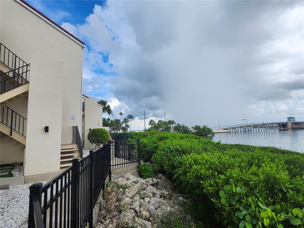 A multi-story building exterior with a metal staircase, black fencing, and a view of water — 1401 BEACH ROAD UNIT 303, ENGLEWOOD, FL