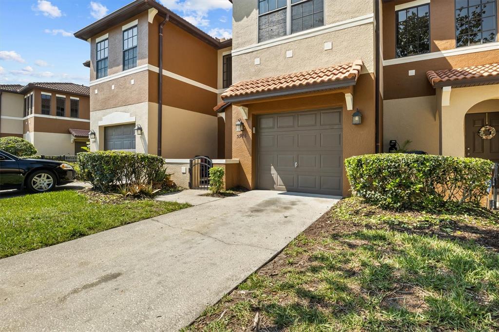 A two-story townhouse exterior features a single-car garage, a concrete driveway, and landscaped bushes — 5986 TIVOLI GARDENS BOULEVARD, ORLANDO, FL