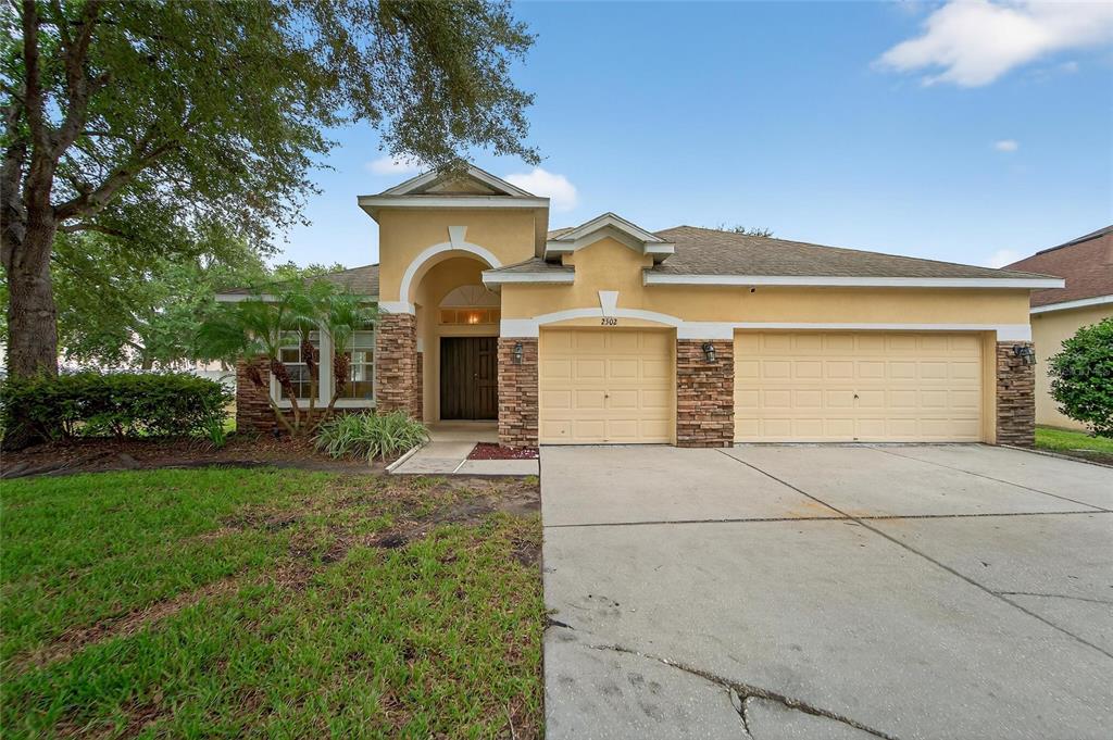 A single-story house with a tan stucco exterior, stone accents, and a three-car garage — 2502 BONTERRA BOULEVARD, VALRICO, FL