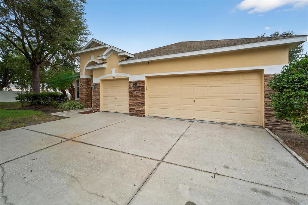 A beige house exterior features a three-car garage, stone accents, and a concrete driveway — 2502 BONTERRA BOULEVARD, VALRICO, FL