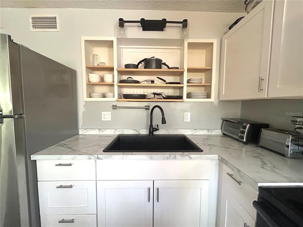 A kitchen with white cabinets, stainless steel appliances, and wood-look flooring opens to a living area — 2275 62ND AVENUE N UNIT 101, ST PETERSBURG, FL