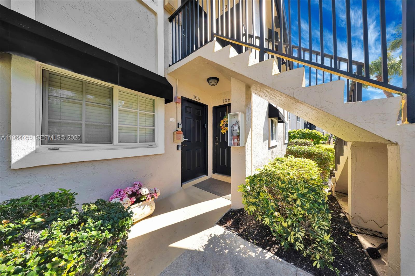 The exterior of a two-story building shows two black apartment doors under a staircase — 4040 Crystal Lake Dr # 105, Deerfield Beach FL 33064, DEERFIELD BEACH, FL