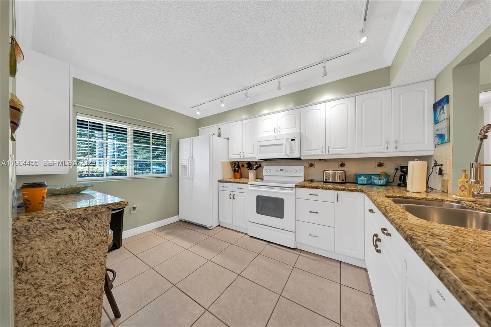 A kitchen features white cabinetry, granite countertops, tile flooring, and a window with blinds — 4040 Crystal Lake Dr # 105, Deerfield Beach FL 33064, DEERFIELD BEACH, FL