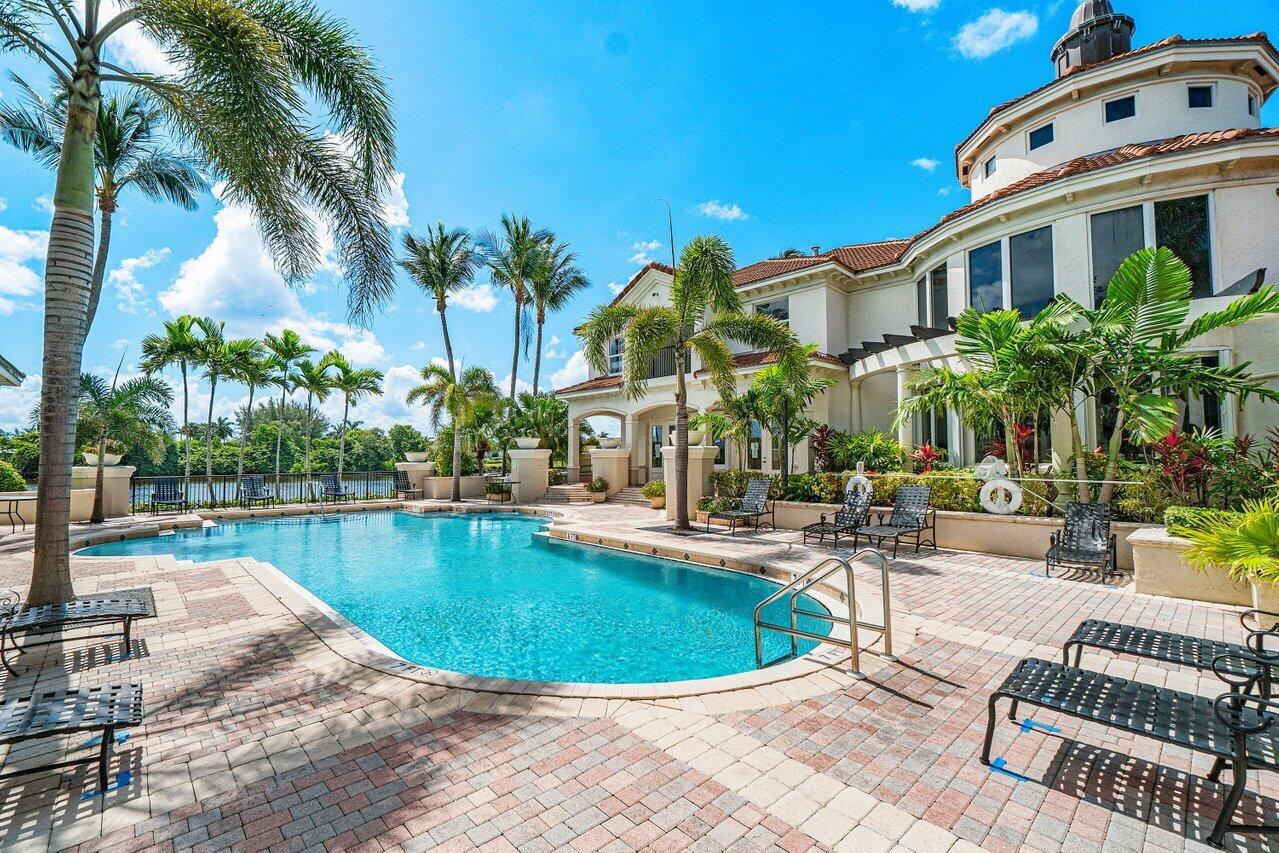 A large swimming pool sits on a brick patio beside a multi-story house with palms — 1302 Tuscany Way, Boynton Beach FL 33435, BOYNTON BEACH, FL