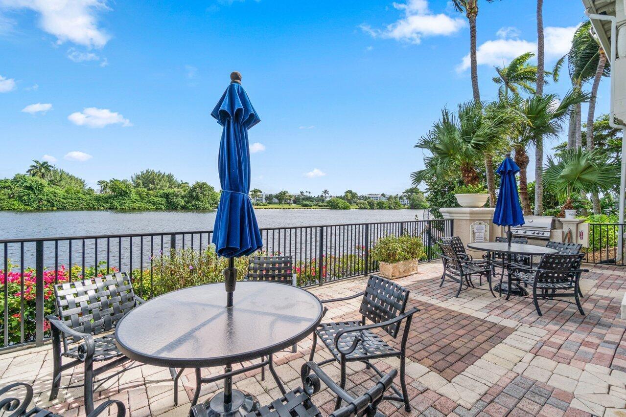 A paved patio with outdoor dining sets overlooks a lake and lush tropical landscaping — 1302 Tuscany Way, Boynton Beach FL 33435, BOYNTON BEACH, FL