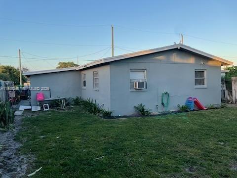 The exterior of a gray, single-story house features a window air conditioning unit and lawn — 1489 W 34th St, Riviera Beach FL 33404, RIVIERA BEACH, FL