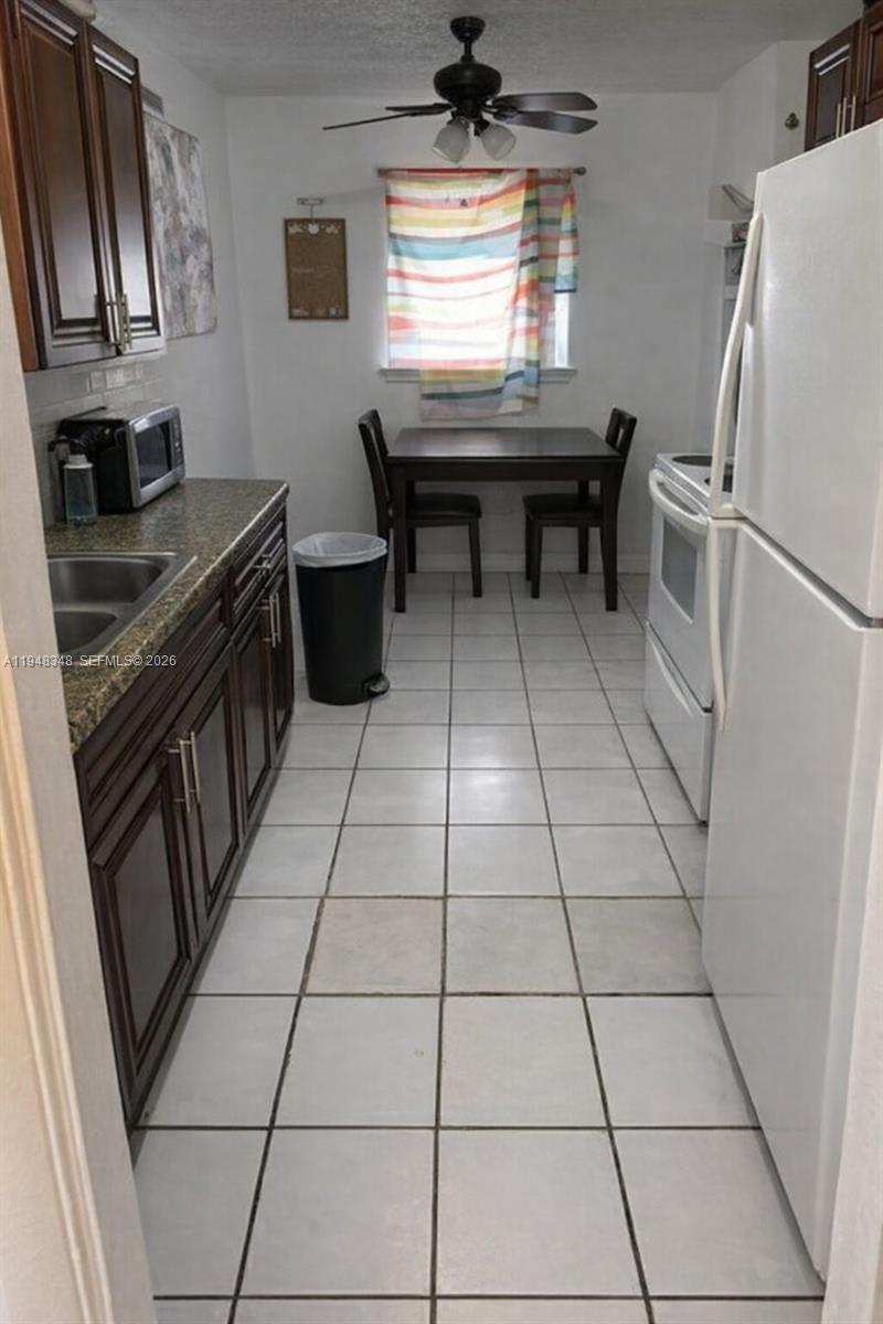 A galley-style kitchen features dark wood cabinets, granite countertops, white appliances, and a dining area — 1489 W 34th St, Riviera Beach FL 33404, RIVIERA BEACH, FL