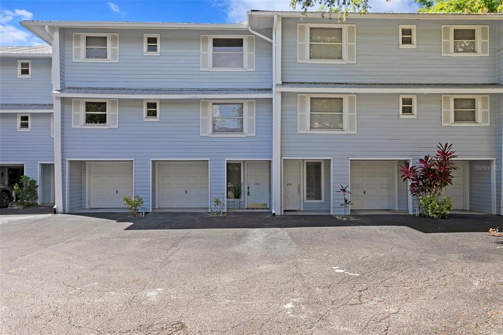 The exterior of a multi-story townhouse complex features light blue siding, white trim, and garages — 4863 W FLAMINGO ROAD UNIT 2, TAMPA, FL