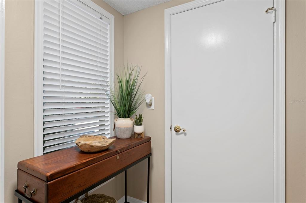 A wooden console table sits beside a white door and a window with blinds — 4863 W FLAMINGO ROAD UNIT 2, TAMPA, FL