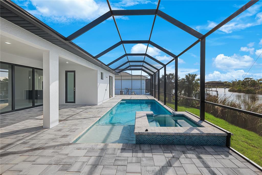 A screened-in pool and spa area with a paved deck overlooking a waterfront view — 10123 BOYLSTON STREET, PORT CHARLOTTE, FL