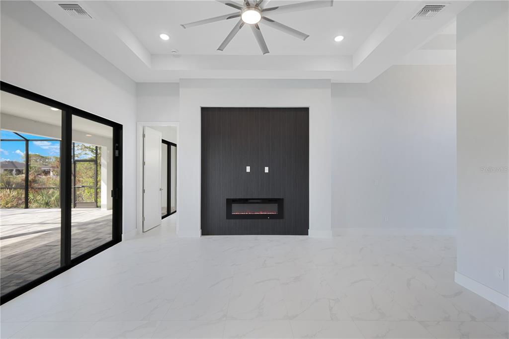 A modern living room features a black slatted fireplace wall, white tile floors, and ceiling fan — 10123 BOYLSTON STREET, PORT CHARLOTTE, FL