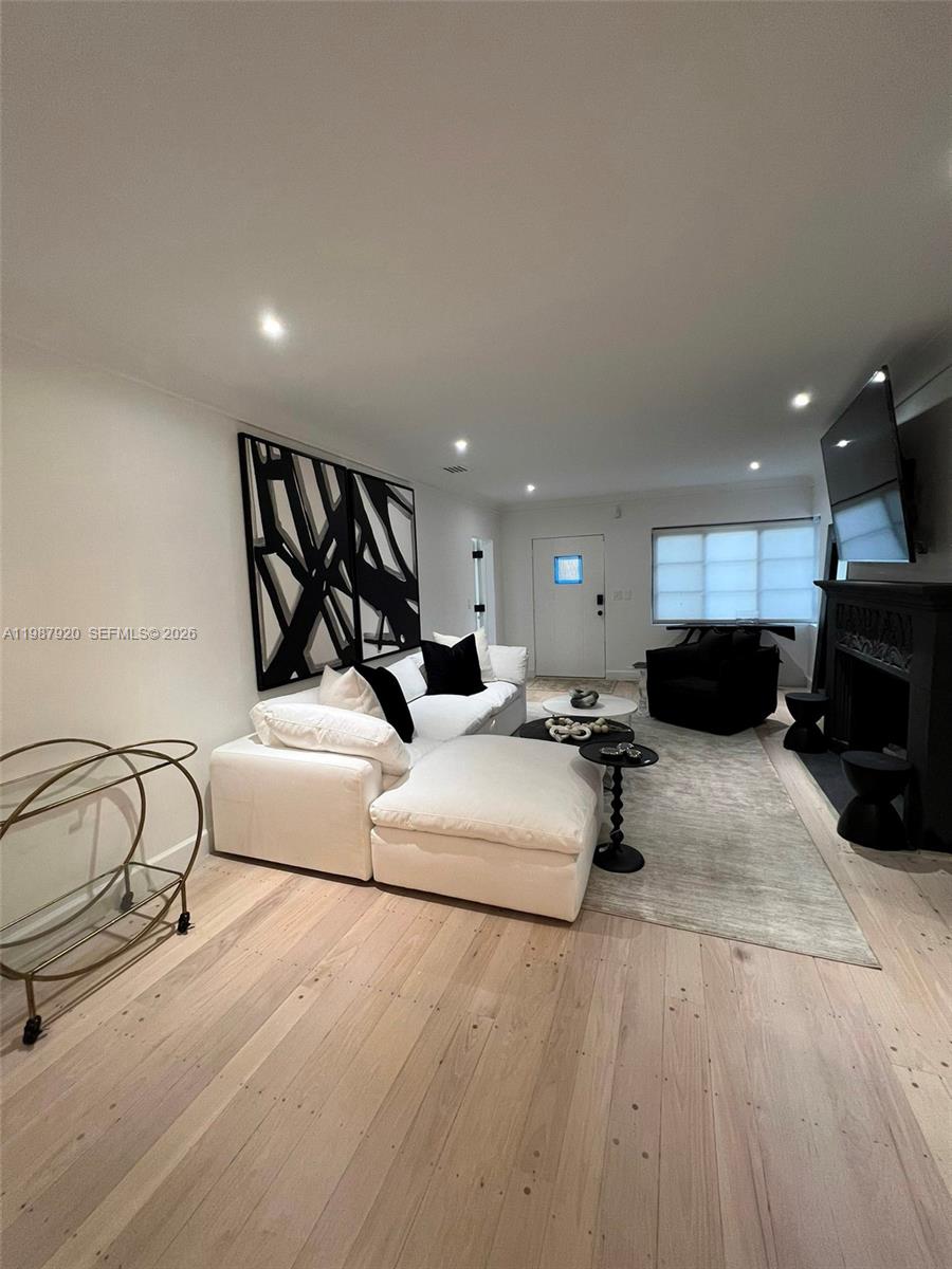 A modern living room features a white sectional sofa, a black fireplace, and light wood floors — 5173 Alton Rd, Miami Beach FL 33140, MIAMI BEACH, FL