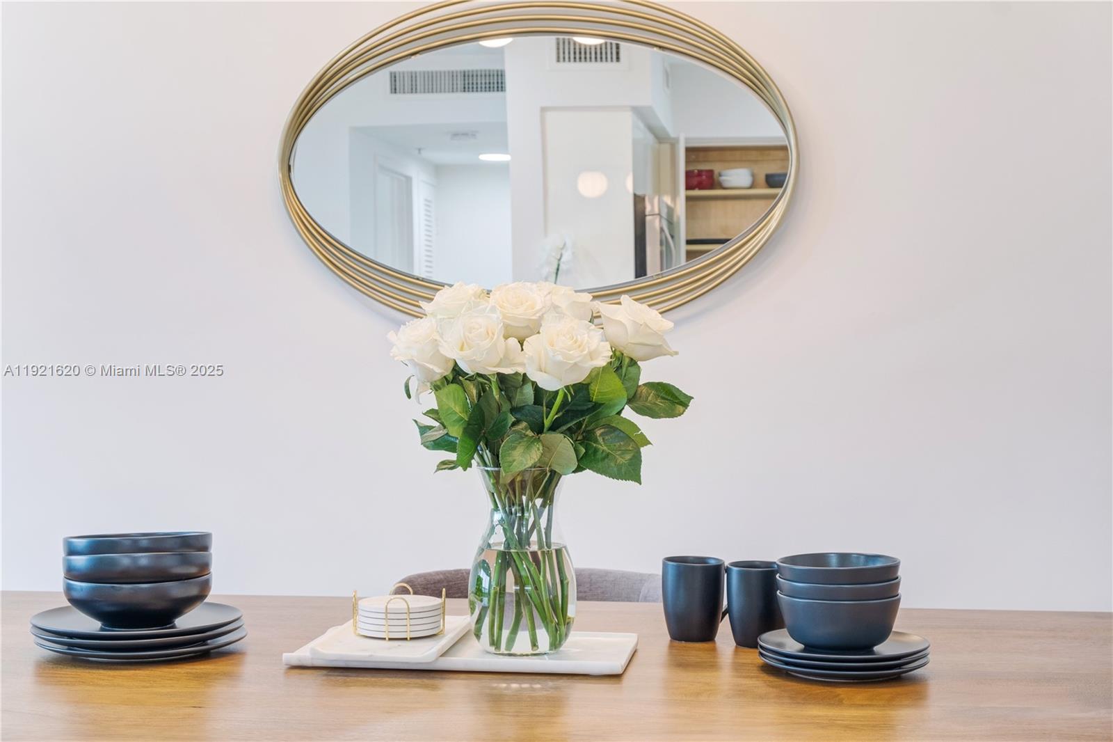A dining table features a vase of white roses, dark bowls, and a wall mirror — 1500 Bay Rd # 1558S, Miami Beach FL 33139, MIAMI BEACH, FL