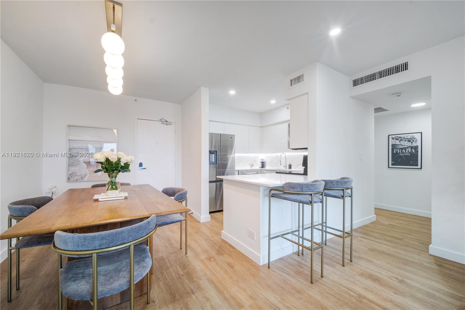 A modern kitchen and dining area features light wood flooring, white cabinetry, and blue chairs — 1500 Bay Rd # 1558S, Miami Beach FL 33139, MIAMI BEACH, FL