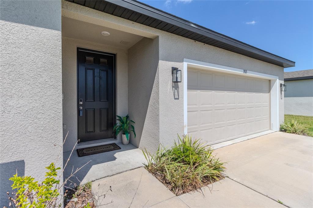 A beige stucco house exterior features a black front door and a tan garage door — 3521 BONSILVA STREET, PLANT CITY, FL