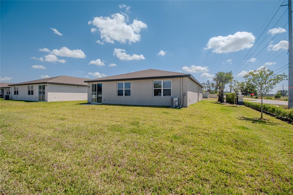 The rear exterior of a beige single-story house with a lawn and sliding glass door — 3521 BONSILVA STREET, PLANT CITY, FL
