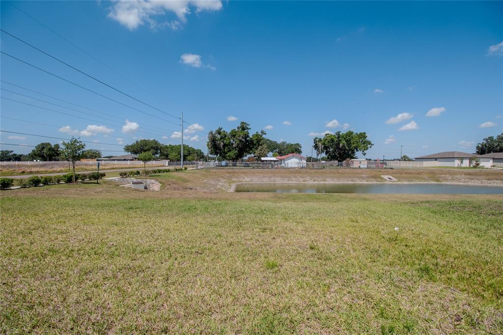 A grassy lawn slopes down toward a retention pond with houses in the background — 3521 BONSILVA STREET, PLANT CITY, FL