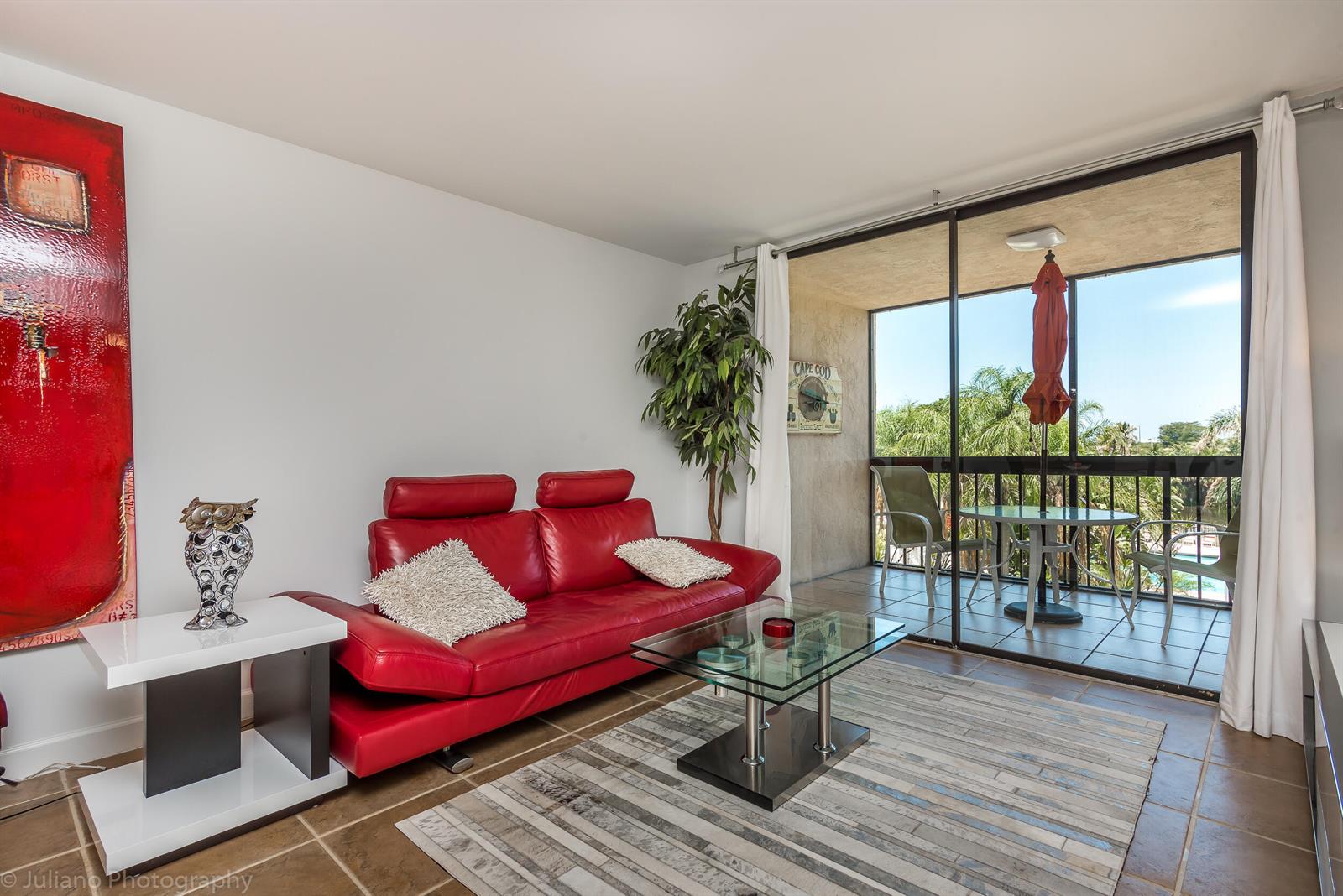 A living room features a red leather sofa, glass coffee table, and a balcony view — 2255 Lindell Boulevard # 4306, Delray Beach FL 33444, DELRAY BEACH, FL
