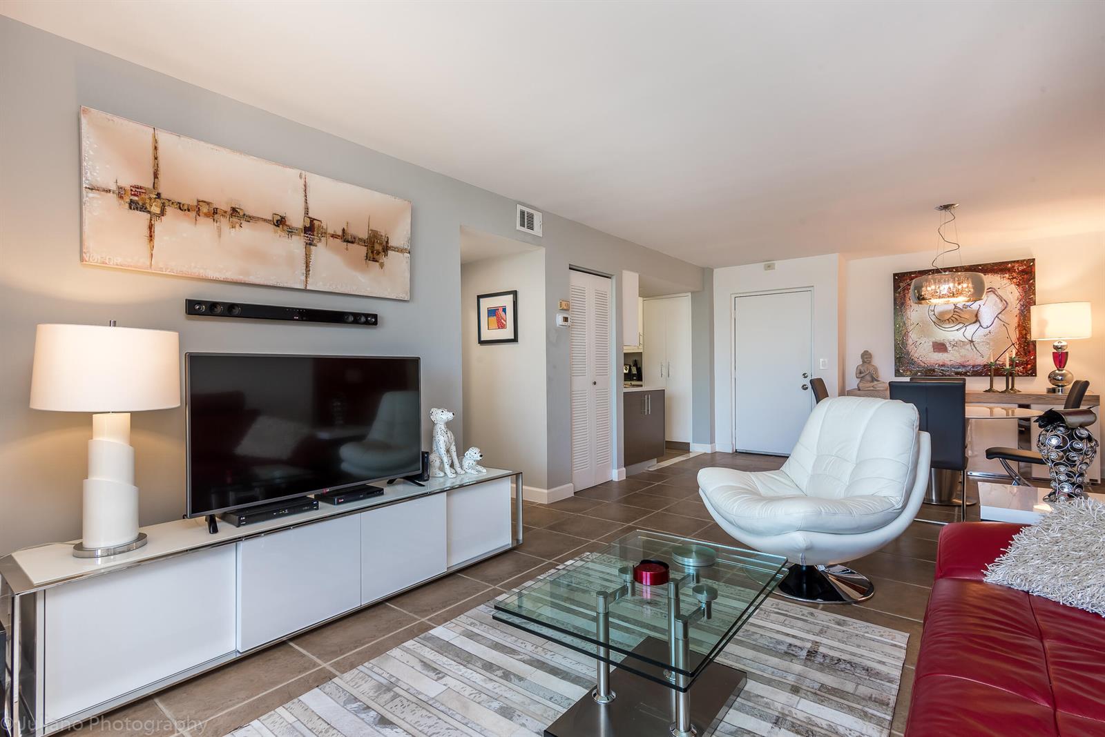 A living room features a white media console, a glass coffee table, and a red sofa — 2255 Lindell Boulevard # 4306, Delray Beach FL 33444, DELRAY BEACH, FL