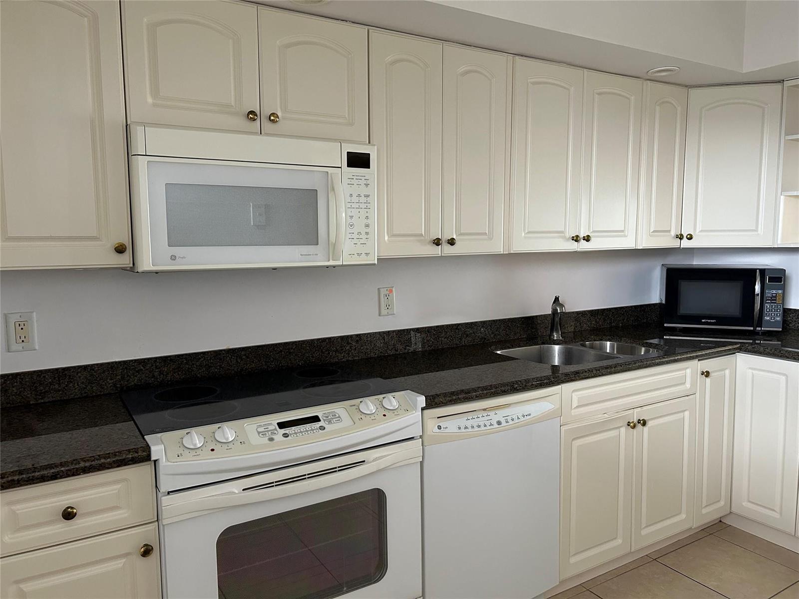 A kitchen features white cabinets, dark granite countertops, and white appliances — 750 N Ocean Boulevard # 1409, Pompano Beach FL 33062, POMPANO BEACH, FL