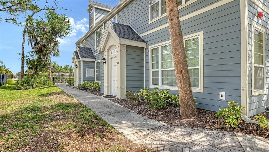 A blue-sided multi-story building features a paved walkway leading to a white front door — 5501 ROSEHILL ROAD UNIT 105, SARASOTA, FL