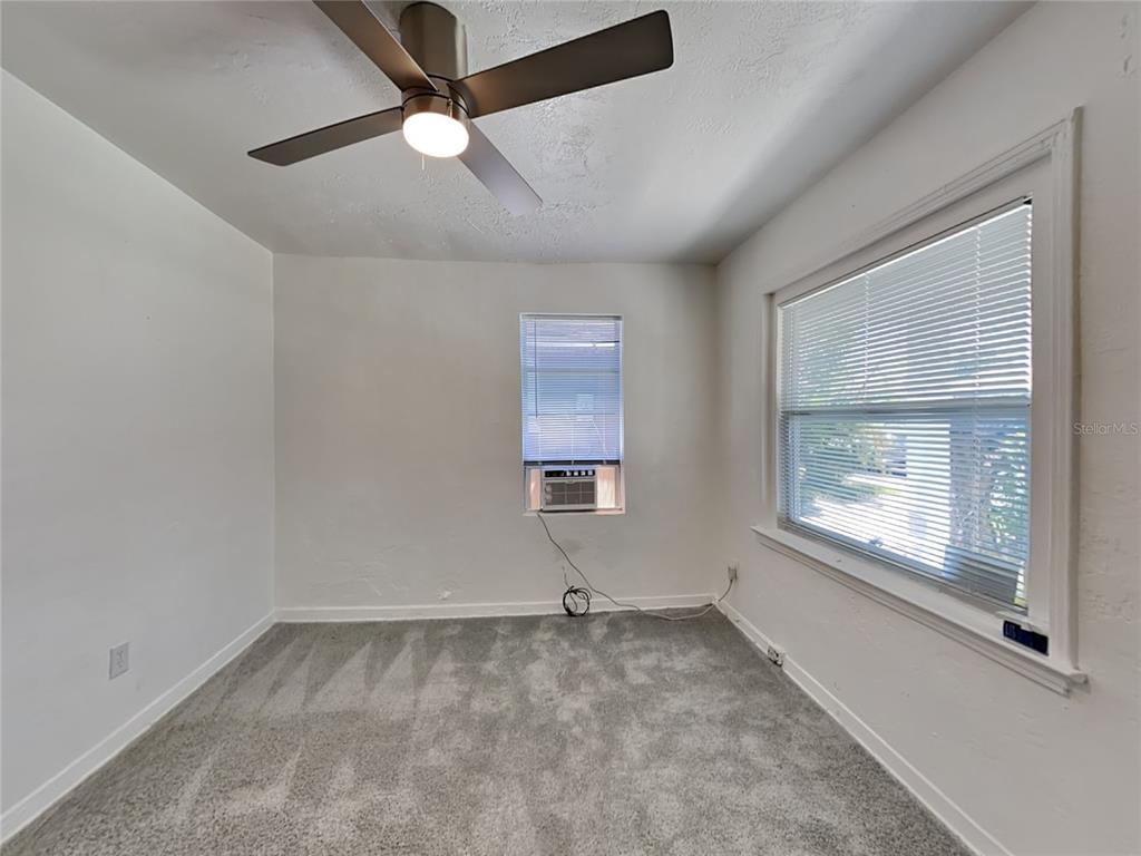 An empty bedroom with gray carpet, white walls, a ceiling fan, and a window air conditioner — 343 PLEASANT STREET UNIT 2, DAYTONA BEACH, FL
