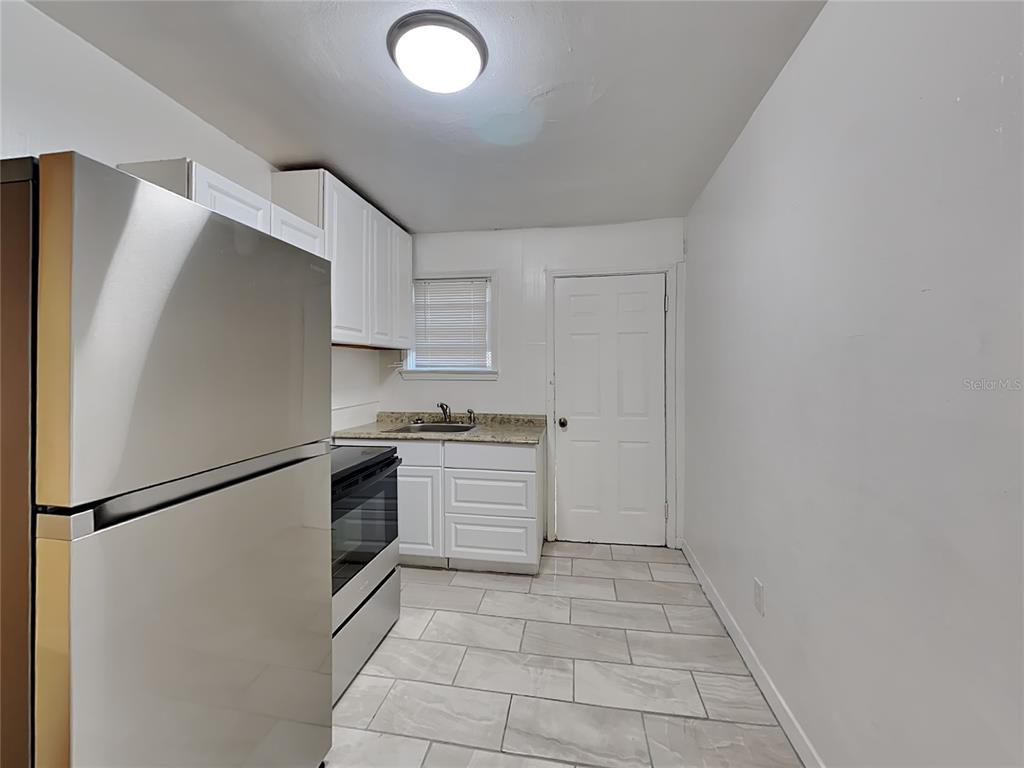A kitchen features white cabinets, stainless steel appliances, granite countertops, and light-colored tile flooring — 343 PLEASANT STREET UNIT 2, DAYTONA BEACH, FL