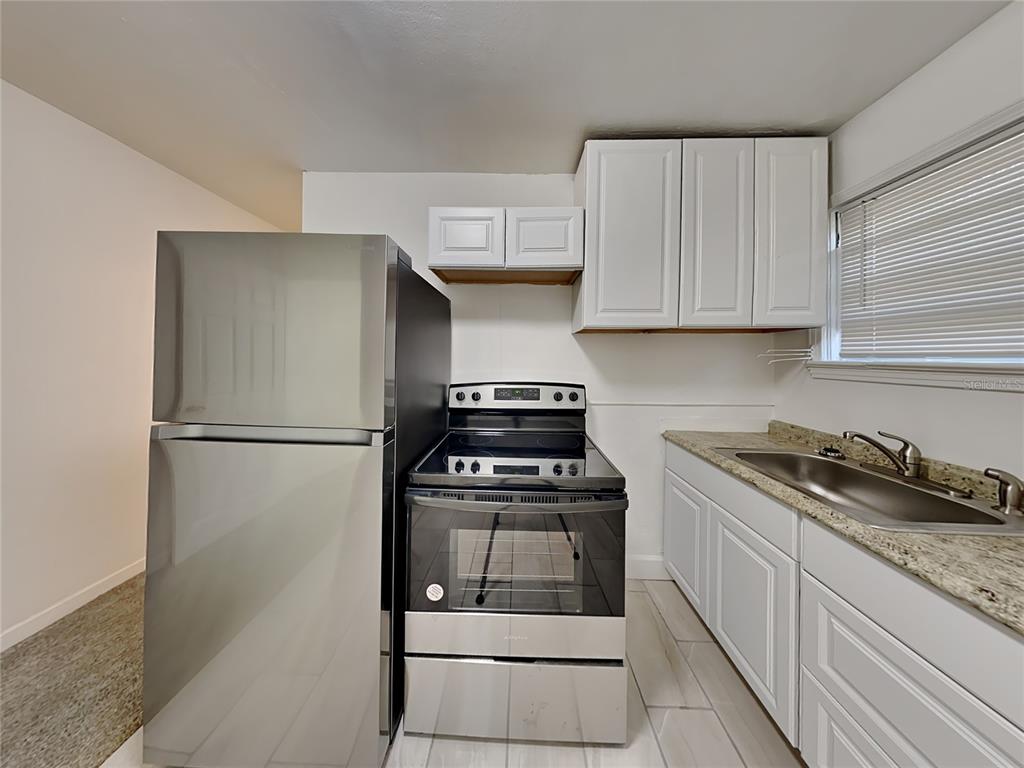 A kitchen features stainless steel appliances, white cabinets, and a granite countertop with a sink — 343 PLEASANT STREET UNIT 2, DAYTONA BEACH, FL