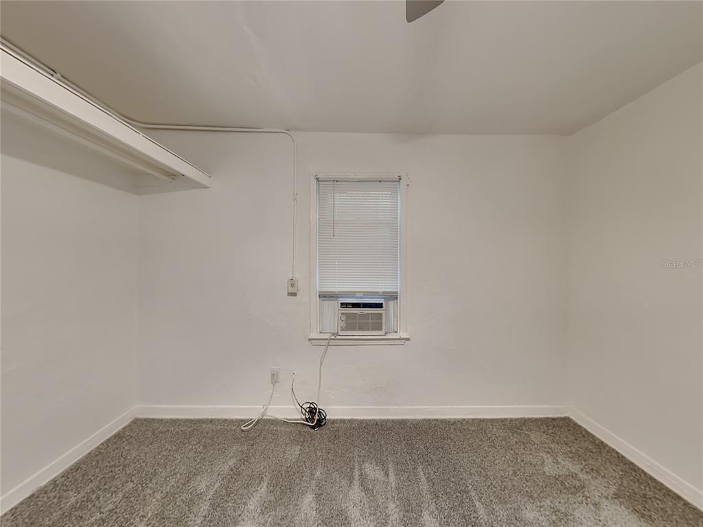 An empty room features gray carpet, white walls, a window air conditioner, and a shelf — 343 PLEASANT STREET UNIT 2, DAYTONA BEACH, FL