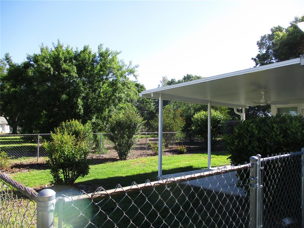 A fenced backyard features a covered patio with a ceiling fan and mature trees — 11565 SW 138TH PLACE, DUNNELLON, FL