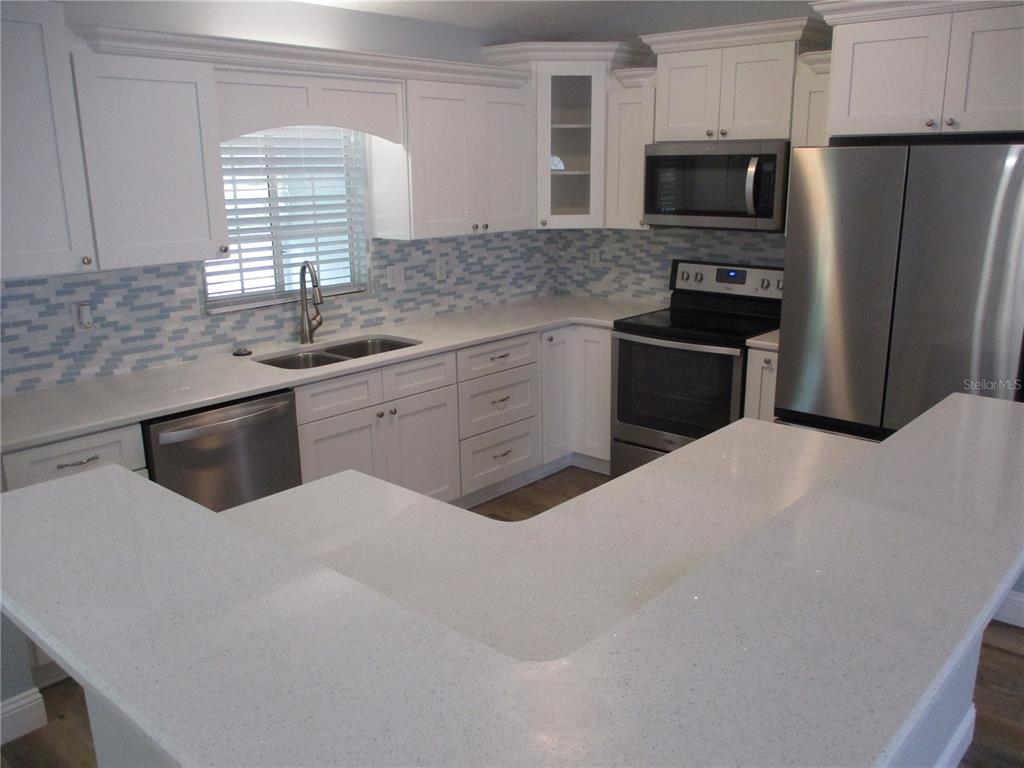 A kitchen features white cabinets, stainless steel appliances, quartz countertops, and a blue tile backsplash — 11565 SW 138TH PLACE, DUNNELLON, FL