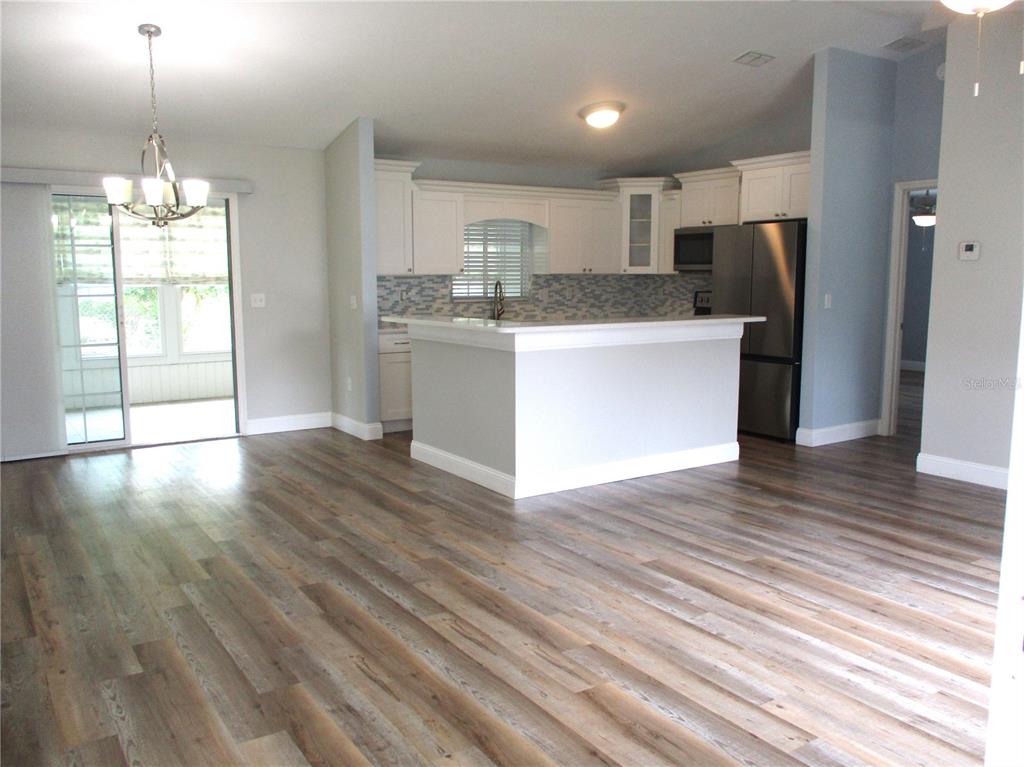 An open-concept kitchen with white cabinets, stainless steel appliances, and wood-look flooring — 11565 SW 138TH PLACE, DUNNELLON, FL