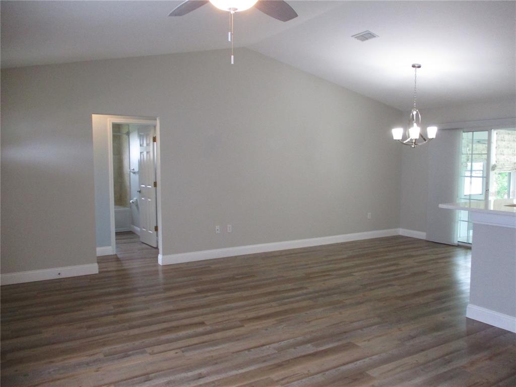 An empty room with light gray walls, wood-look flooring, a vaulted ceiling, and a chandelier — 11565 SW 138TH PLACE, DUNNELLON, FL
