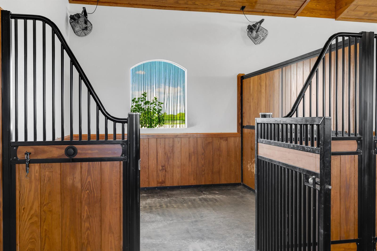 A horse stall with wooden walls, black metal gates, and a window with chain curtains — 5181 Lasso Way, Wellington FL 33449, WELLINGTON, FL