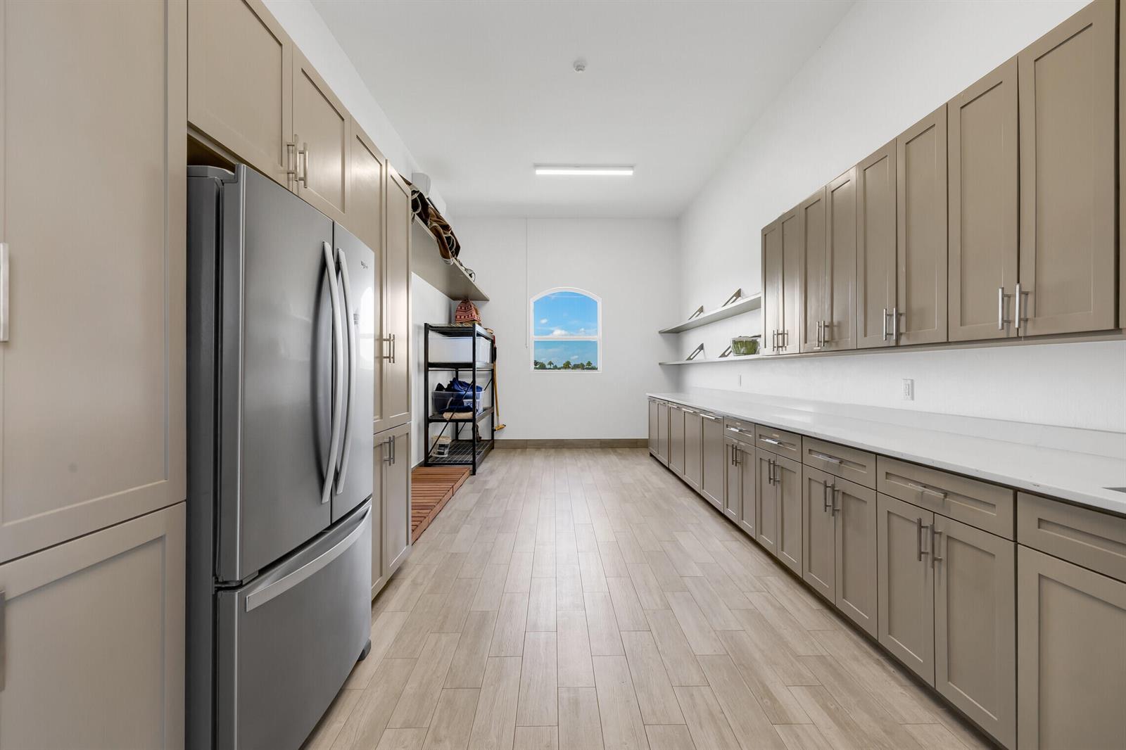 A long utility room features light wood-look tile floors, taupe cabinetry, and a stainless refrigerator — 5181 Lasso Way, Wellington FL 33449, WELLINGTON, FL