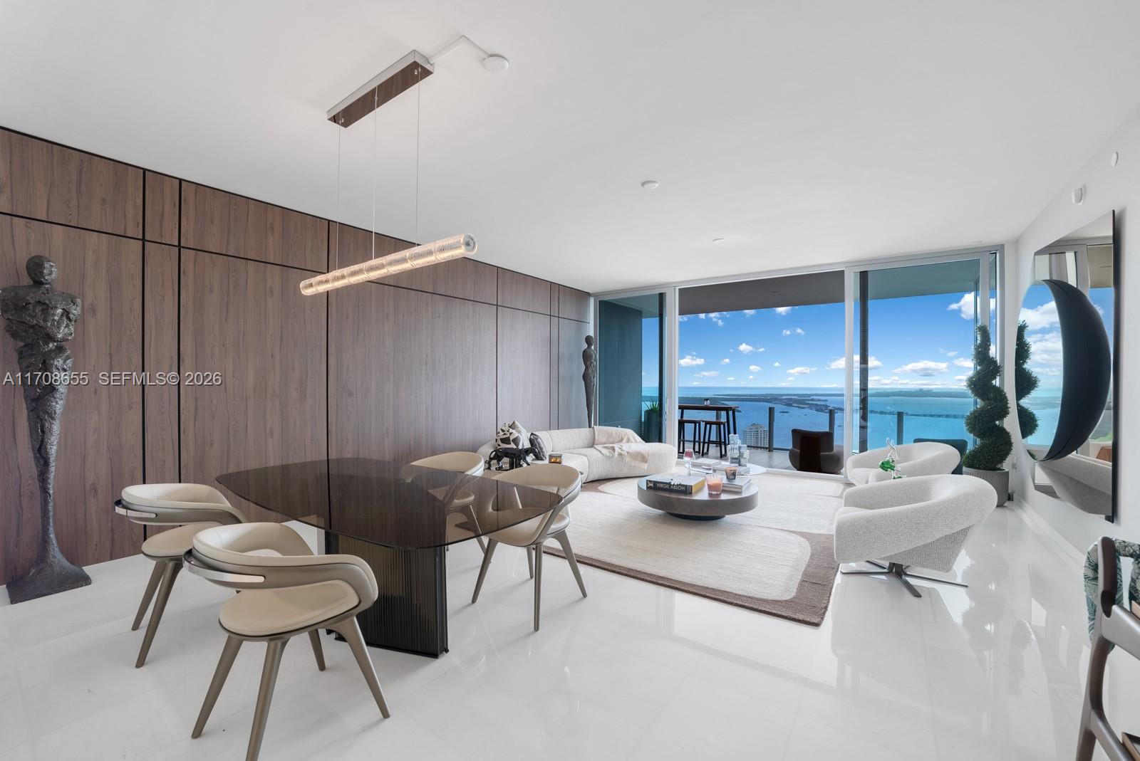 A modern living and dining area features wood-paneled walls, white floors, and floor-to-ceiling ocean views — 300 Biscayne Blvd Way # 4703, Miami FL 33131, MIAMI, FL