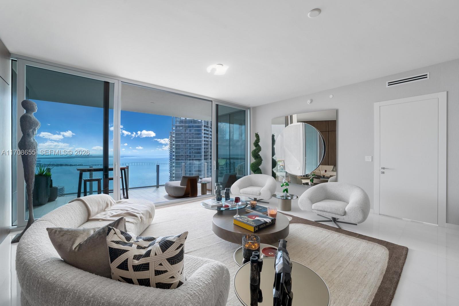 A modern living room features a curved sofa, two armchairs, and floor-to-ceiling windows overlooking water — 300 Biscayne Blvd Way # 4703, Miami FL 33131, MIAMI, FL