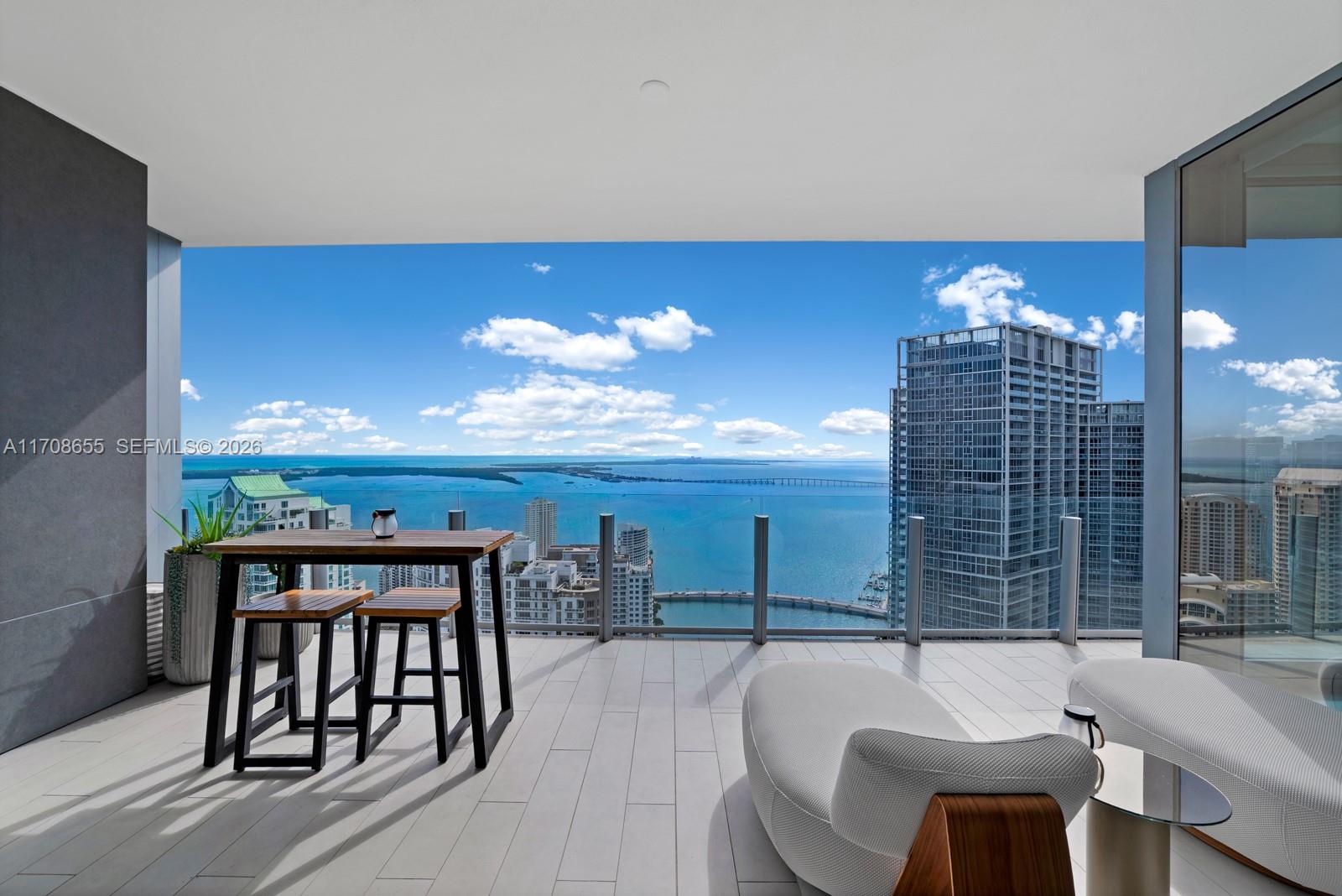 A high-rise balcony features a dining set, lounge chairs, and an expansive ocean view — 300 Biscayne Blvd Way # 4703, Miami FL 33131, MIAMI, FL