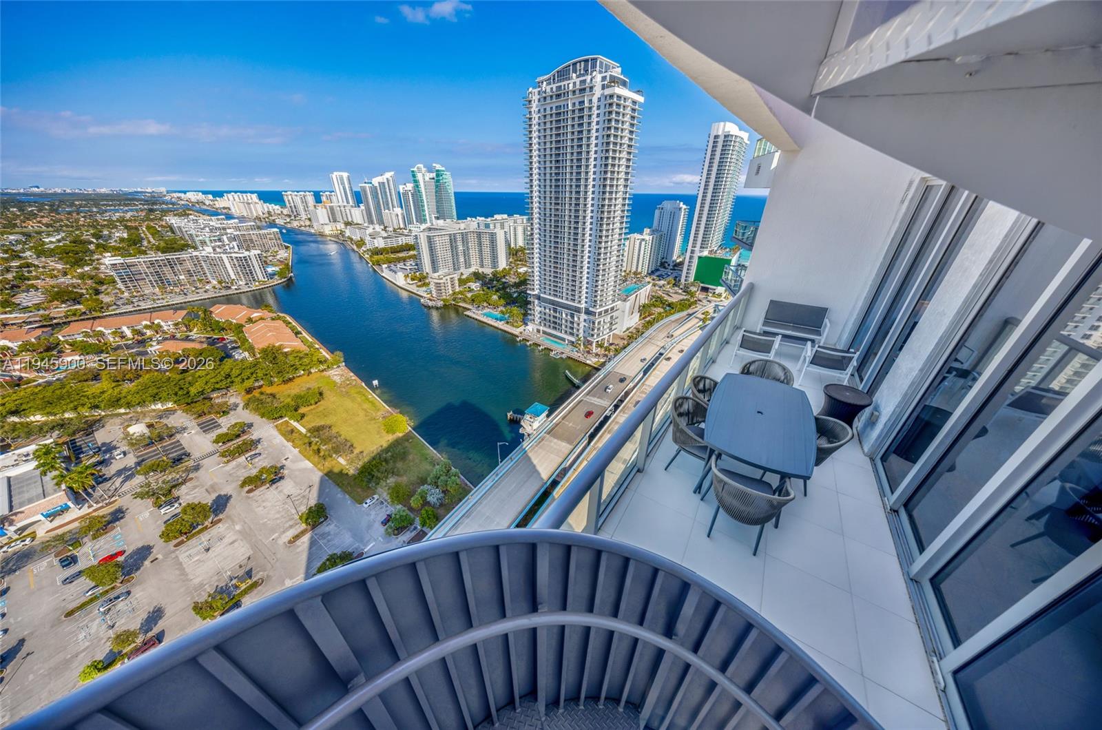 A high-rise balcony with outdoor furniture overlooks a canal, a bridge, and city skyscrapers — 2600 E Hallandale Beach Blvd # T3304, Hallandale Beach FL 33009, HALLANDALE BEACH, FL