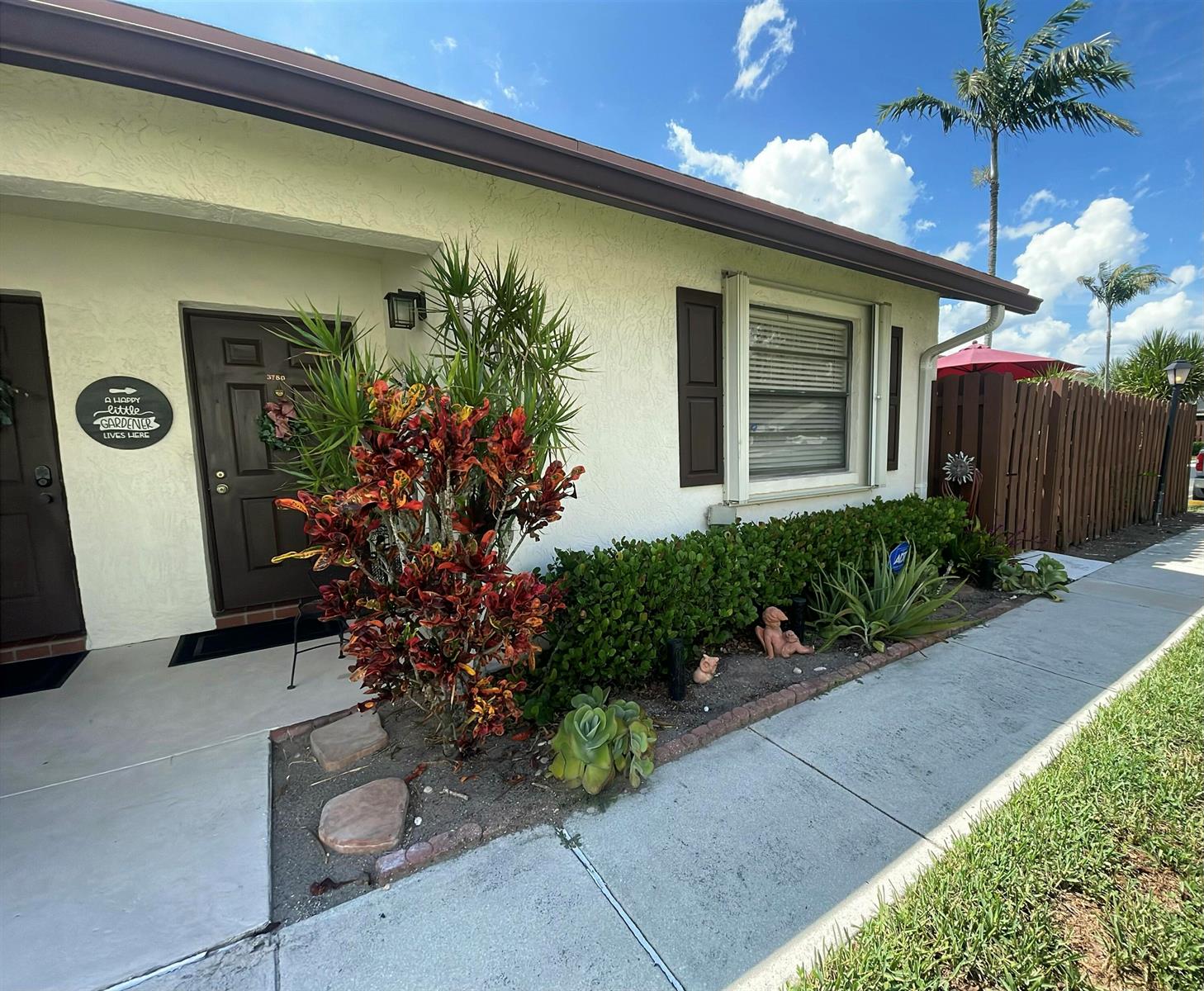 A single-story house exterior features a brown door, a croton plant, and a landscaped garden — 3780 Lace Vine Lane # 131, Boynton Beach FL 33436, BOYNTON BEACH, FL