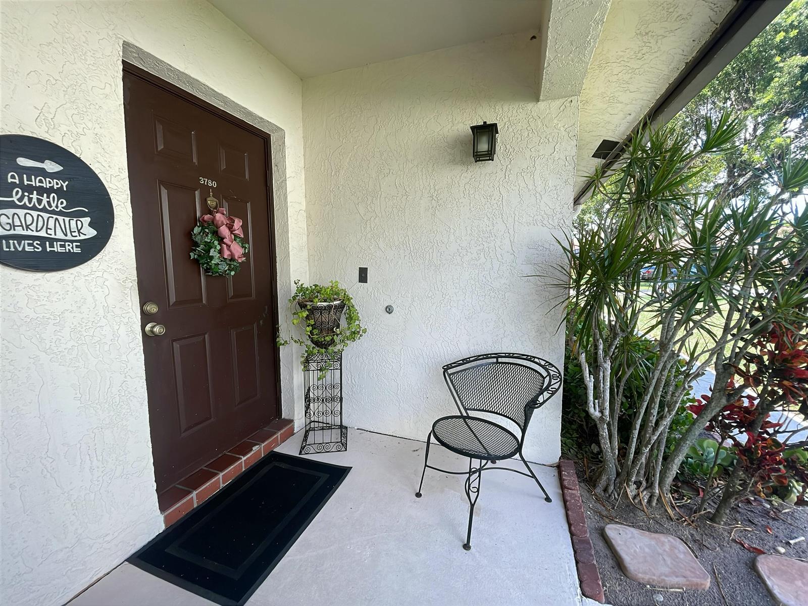 A brown front door with a wreath and a metal chair sit on a porch — 3780 Lace Vine Lane # 131, Boynton Beach FL 33436, BOYNTON BEACH, FL