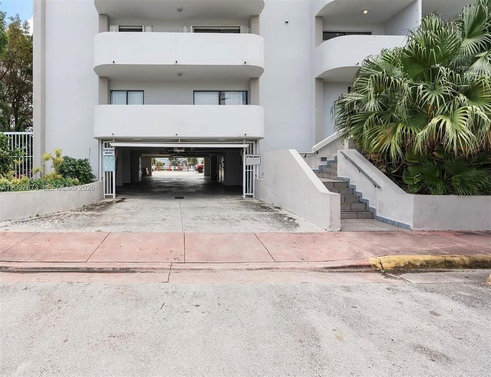 An exterior view of an apartment building with a ground-level parking garage and concrete stairs — 110 S Shore Dr # 5B, Miami Beach FL 33141, MIAMI BEACH, FL