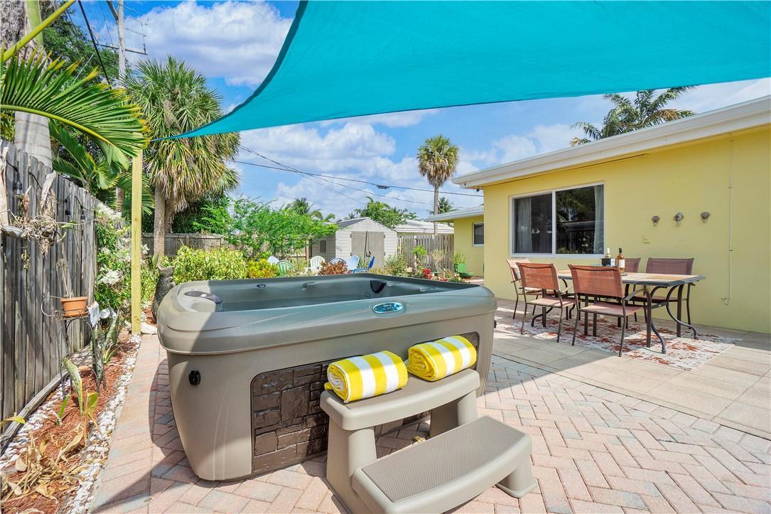 A hot tub with yellow-striped towels sits on a paved patio beside an outdoor dining set — 161 SE 5th Court, Pompano Beach FL 33060, POMPANO BEACH, FL