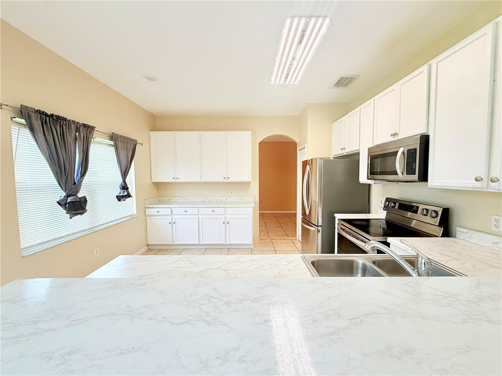 A kitchen features white cabinets, marble-look countertops, stainless steel appliances, and a double sink — 4208 LUGANO COURT, KISSIMMEE, FL