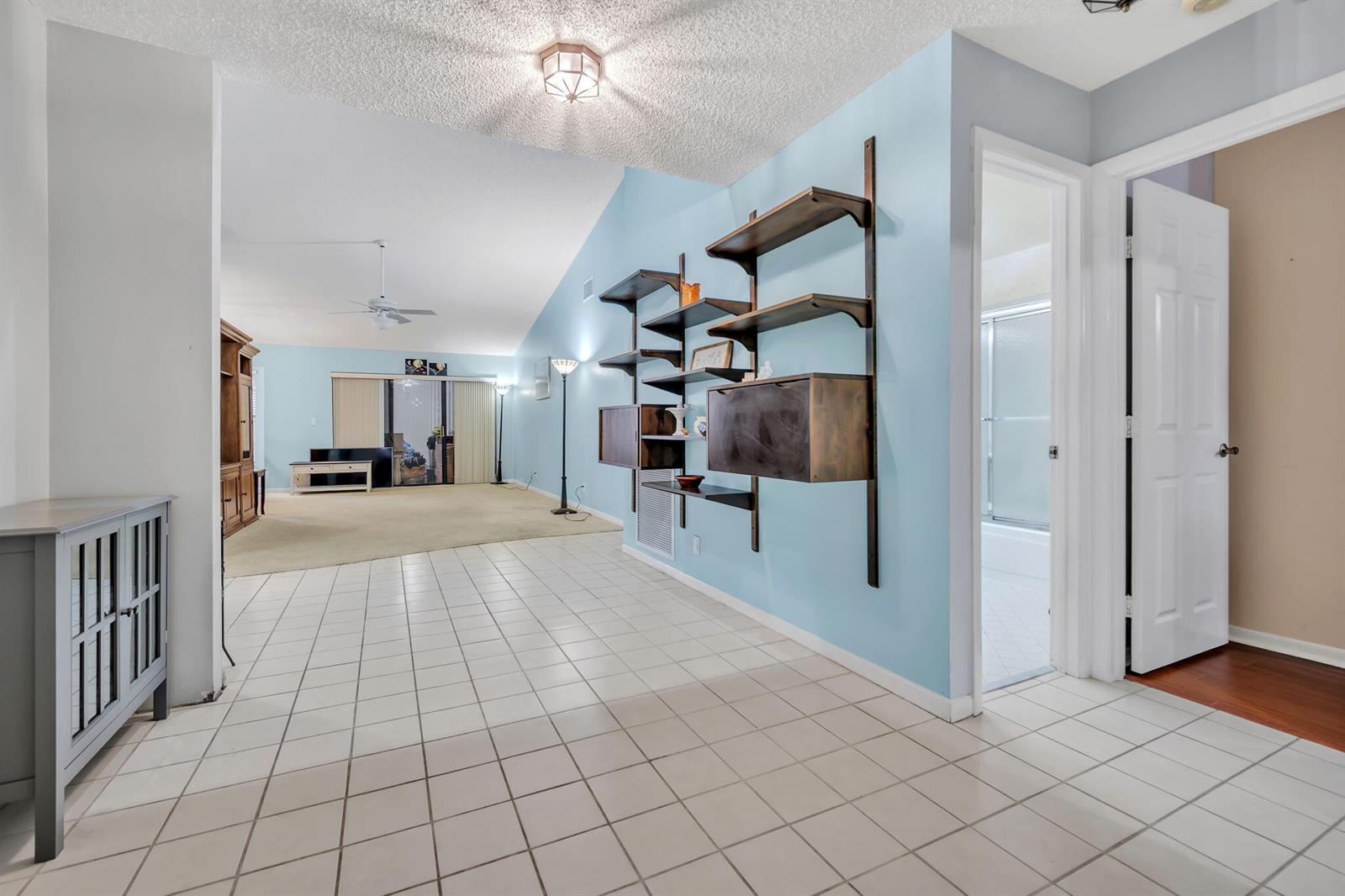 A tiled entryway leads into a living room with light blue walls and wall-mounted shelving — 2643 Calliandra Terrace, Coconut Creek FL 33063, COCONUT CREEK, FL